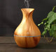 Difusor de aroma de madera Sabi Equilibrio en mesa, planta verde al fondo.